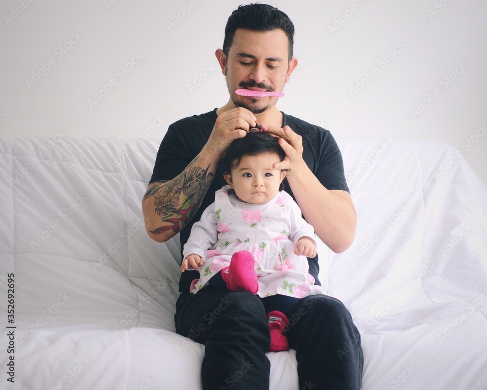 Joven padre peinando el cabello de su bebé Padre con peine en la boca  haciendo un moño al cabello de su hija Día del padre foto de Stock   Adobe Stock