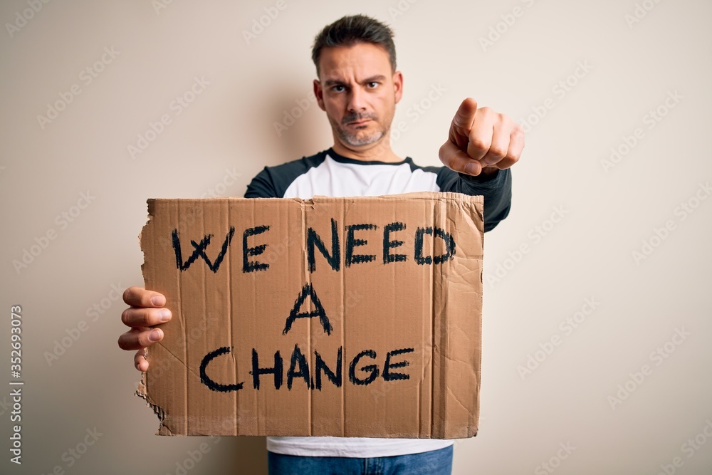 Young handsome activist man holding banner with change message over pink background pointing with finger to the camera and to you, hand sign, positive and confident gesture from the front Young handsome activist man holding banner with change message over pink background pointing with finger to the camera and to you, hand sign, positive and confident gesture from the front