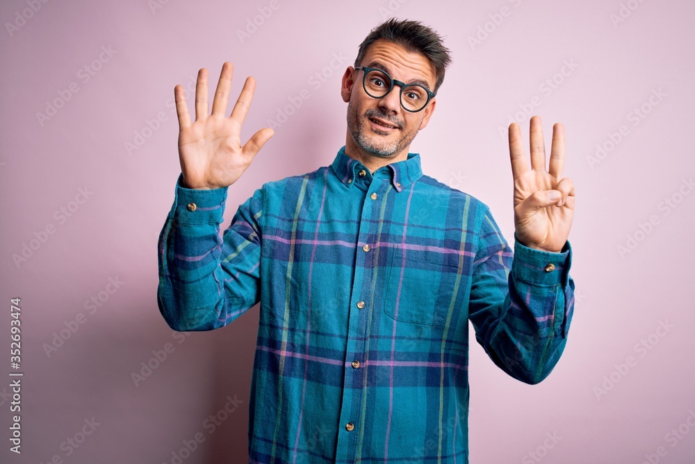 Young handsome man wearing casual shirt and glasses standing over isolated pink background showing and pointing up with fingers number eight while smiling confident and happy. Young handsome man wearing casual shirt and glasses standing over isolated pink background showing and pointing up with fingers number eight while smiling confident and happy.
