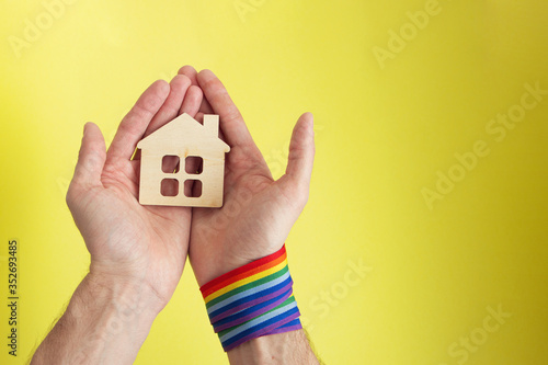 male hands with rainbow gay pride LGBT ribbon wristband holding small wooden house