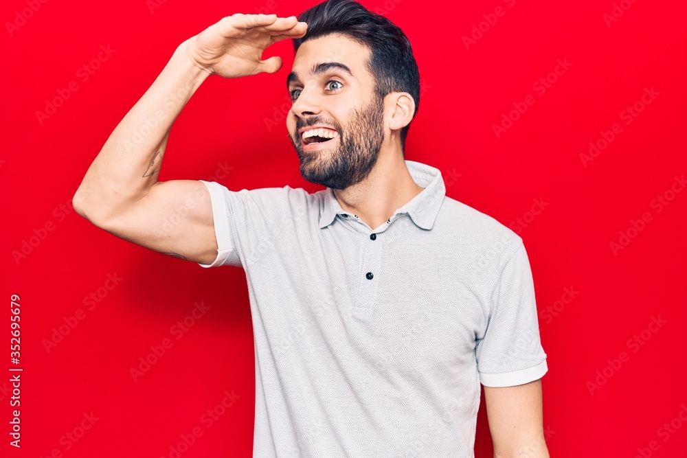 Young handsome man with beard wearing casual polo very happy and smiling looking far away with hand over head. searching concept. Young handsome man with beard wearing casual polo very happy and smiling looking far away with hand over head. searching concept.