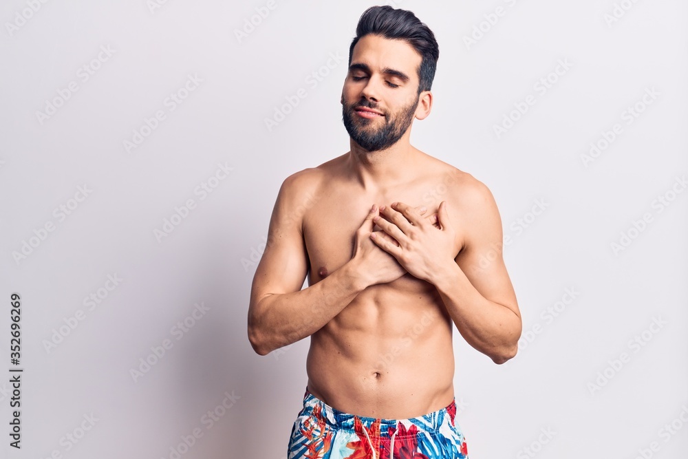 Young handsome man with beard shirtless wearing swimwear smiling with hands on chest, eyes closed with grateful gesture on face. health concept.