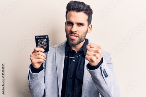Young handsome man with beard holding police badge annoyed and frustrated shouting with anger, yelling crazy with anger and hand raised © Krakenimages.com
