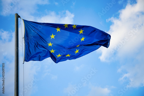 Flag of the European Union on a flagpole waving against a blue sky