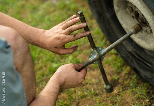 a man unscrews the nuts on the wheel of a car with a wheel wrench