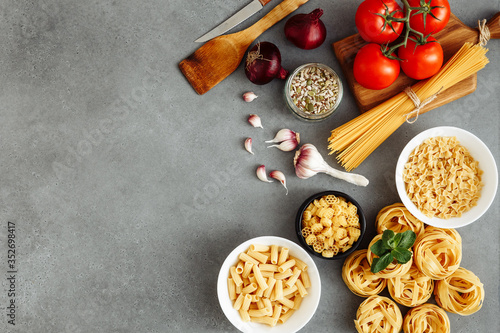 Spaghetti and fettuccine with ingredients for cooking pasta on gray table, top view from above. Rustic style. Onion, pasta, garlic, seasoning, pasta. Flat lay