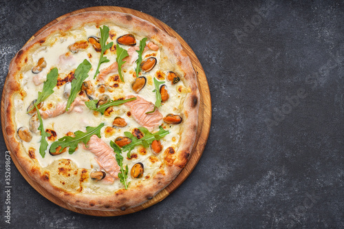 Seafood pizza, marinara, di mare, with salmon, mussels and arugula, on a wooden board, against a dark background