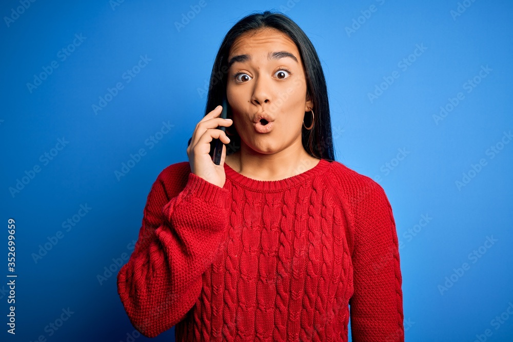 Young beautiful asian woman having conversation talking on smartphone over blue background scared in shock with a surprise face, afraid and excited with fear expression Young beautiful asian woman having conversation talking on smartphone over blue background scared in shock with a surprise face, afraid and excited with fear expression