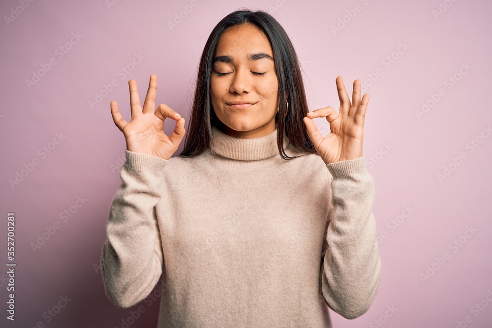 Young beautiful asian woman wearing casual turtleneck sweater over pink background relax and smiling with eyes closed doing meditation gesture with fingers. Yoga concept. Young beautiful asian woman wearing casual turtleneck sweater over pink background relax and smiling with eyes closed doing meditation gesture with fingers. Yoga concept.