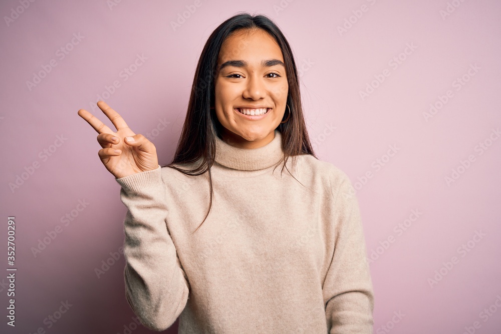 Young beautiful asian woman wearing casual turtleneck sweater over pink background showing and pointing up with fingers number two while smiling confident and happy. Young beautiful asian woman wearing casual turtleneck sweater over pink background showing and pointing up with fingers number two while smiling confident and happy.