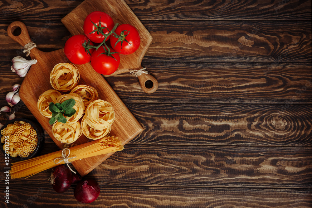 Dried mixed pasta, vegetables, kitchen cutting board on the dark wooden table, top view, flat lay with copy space. Dried mixed pasta, vegetables, kitchen cutting board on the dark wooden table, top view, flat lay with copy space.