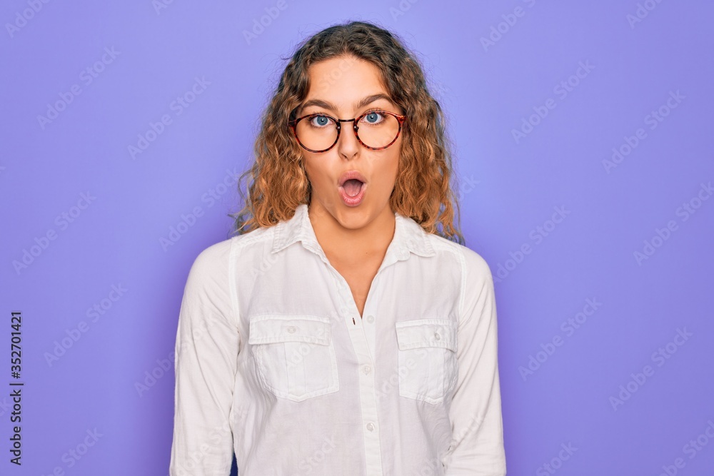 Young beautiful woman with blue eyes wearing casual shirt and glasses over purple background afraid and shocked with surprise expression, fear and excited face.