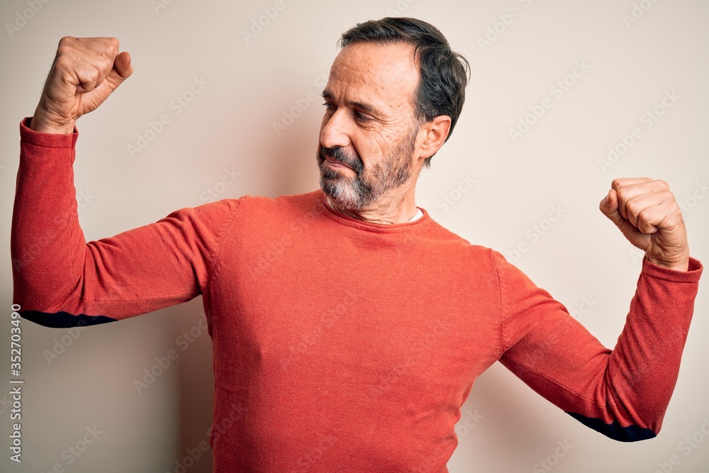 Middle age hoary man wearing casual orange sweater standing over isolated white background showing arms muscles smiling proud. Fitness concept. Middle age hoary man wearing casual orange sweater standing over isolated white background showing arms muscles smiling proud. Fitness concept.