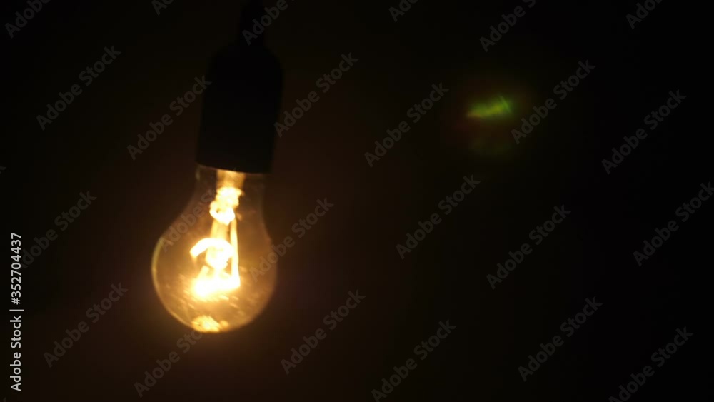 Classic glass lamp with tungsten filament flicker lights up, swaying on the wire on a black background. Closeup. Slow mo, slo mo, slow motion, high speed camera Classic glass lamp with tungsten filament flicker lights up, swaying on the wire on a black background. Closeup. Slow mo, slo mo, slow motion, high speed camera