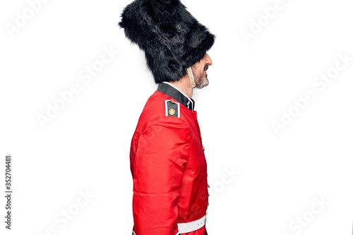 Middle age handsome wales guard man wearing traditional uniform over white background looking to side, relax profile pose with natural face and confident smile.