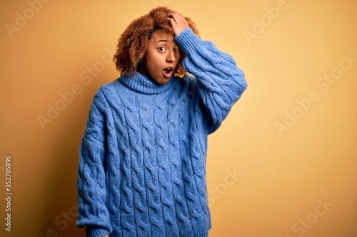 Young beautiful African American afro woman with curly hair wearing blue turtleneck sweater surprised with hand on head for mistake, remember error. Forgot, bad memory concept. © Krakenimages.com