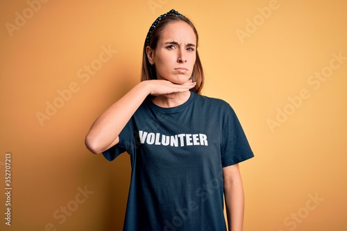 Young beautiful woman wearing volunteer t-shirt doing volunteering over yellow background cutting throat with hand as knife, threaten aggression with furious violence