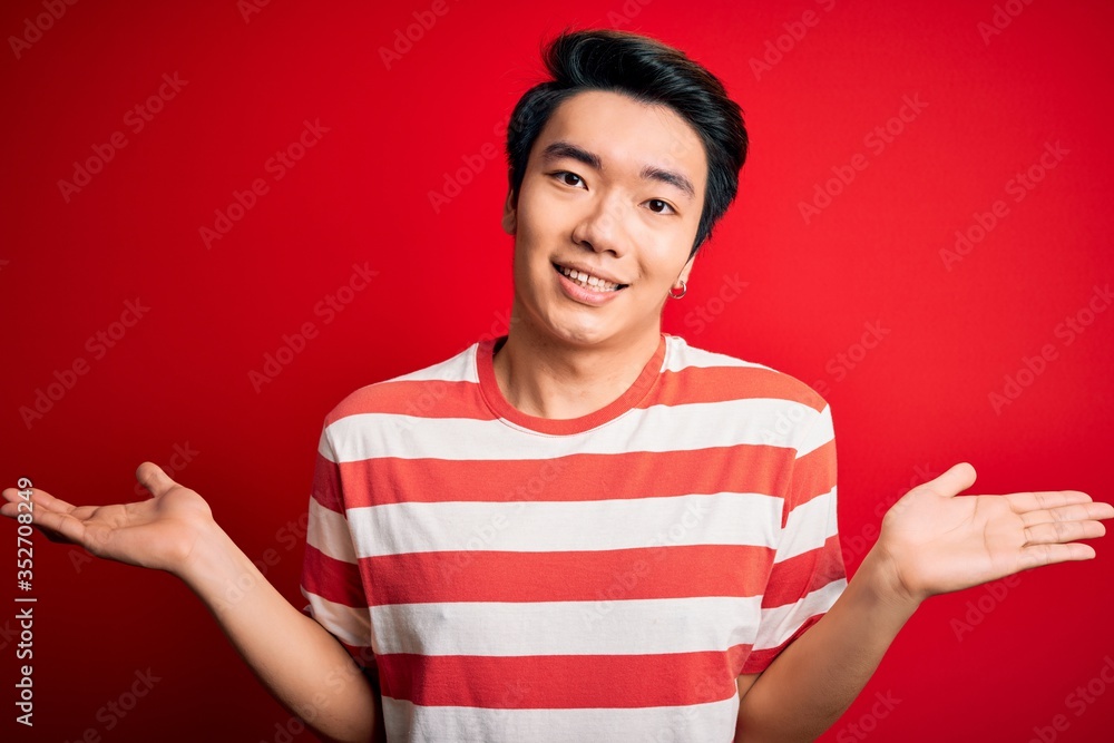 Young handsome chinese man wearing casual striped t-shirt standing over red background smiling showing both hands open palms, presenting and advertising comparison and balance Young handsome chinese man wearing casual striped t-shirt standing over red background smiling showing both hands open palms, presenting and advertising comparison and balance