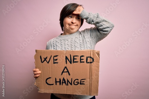 Young down syndrome woman holding protest banner we need a change from political problems stressed with hand on head, shocked with shame and surprise face, angry and frustrated. Fear and upset © Krakenimages.com