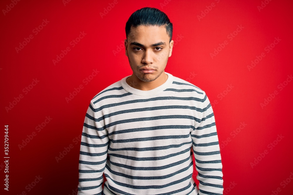 Young brazilian man wearing casual striped t-shirt standing over isolated red background depressed and worry for distress, crying angry and afraid. Sad expression. Young brazilian man wearing casual striped t-shirt standing over isolated red background depressed and worry for distress, crying angry and afraid. Sad expression.