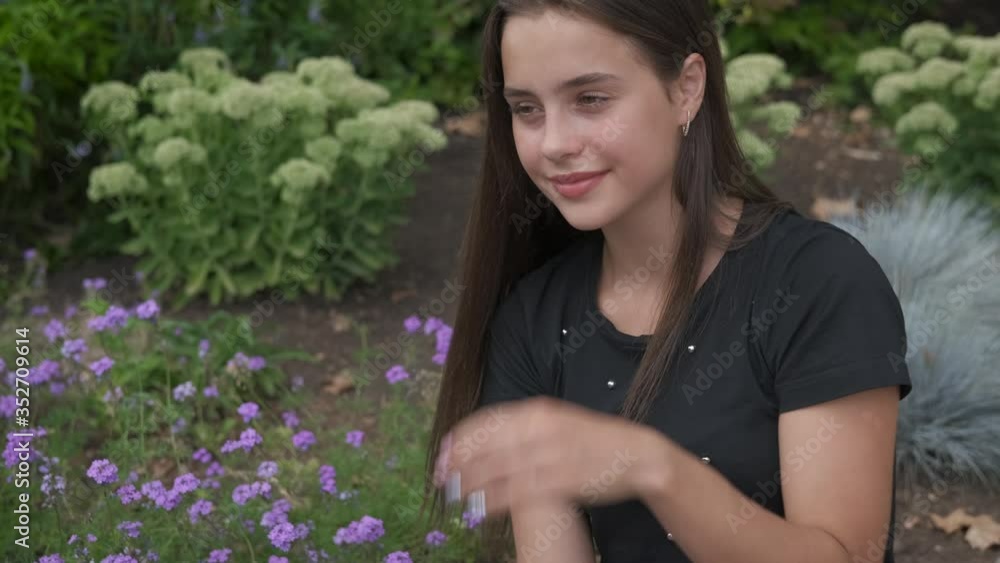 The girl at the flower bed. A cute young girl looks at flowers in the summer garden. The girl at the flower bed. A cute young girl looks at flowers in the summer garden.