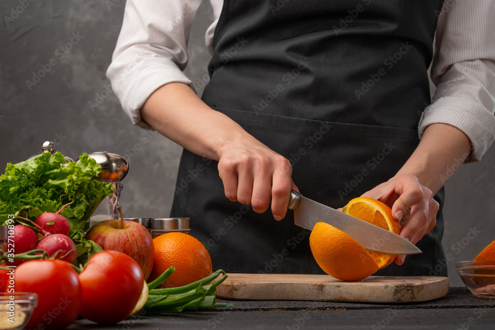 Chef cuts oranges for cooking dishes on the background of the ingredients of vegetables and fruits. Useful and proper nutrition Chef cuts oranges for cooking dishes on the background of the ingredients of vegetables and fruits. Useful and proper nutrition