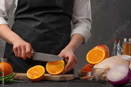 Chef cuts oranges for cooking festive chicken. Against the background of vegetables