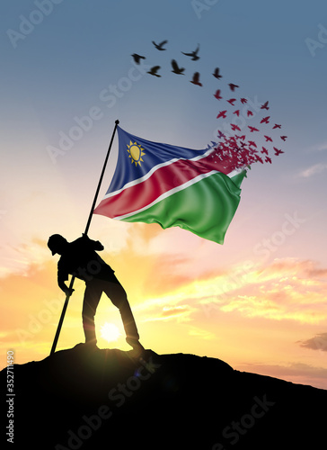 Namibia flag turn to birds while being planted by a man on a hill during sunrise.