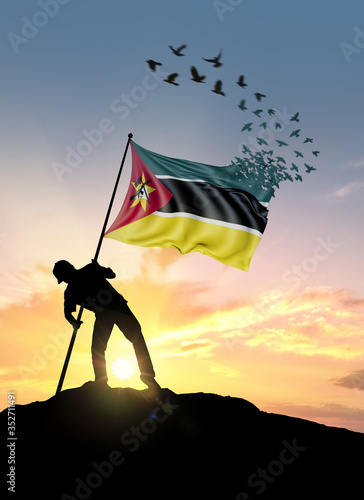 Canvas Print Mozambique flag turn to birds while being planted by a man on a hill during sunrise