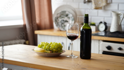 Close up of open bottle of wine and glass of wine with fruits on plate on table in kitchen. Concept of dating.