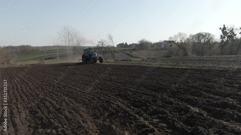Wide shot of agricultural tractor furrowing fertile field on sunny spring day. Machinery working under blue spring sky. Concept of farming, agronomy, agriculture, gardening. Wide shot of agricultural tractor furrowing fertile field on sunny spring day. Machinery working under blue spring sky. Concept of farming, agronomy, agriculture, gardening.