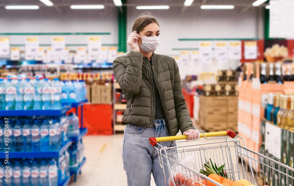 Social distancing in a supermarket. A young woman in a disposable face masks and gloves with grocery basket. Shopping during the Coronavirus Covid-19 epidemic 2020