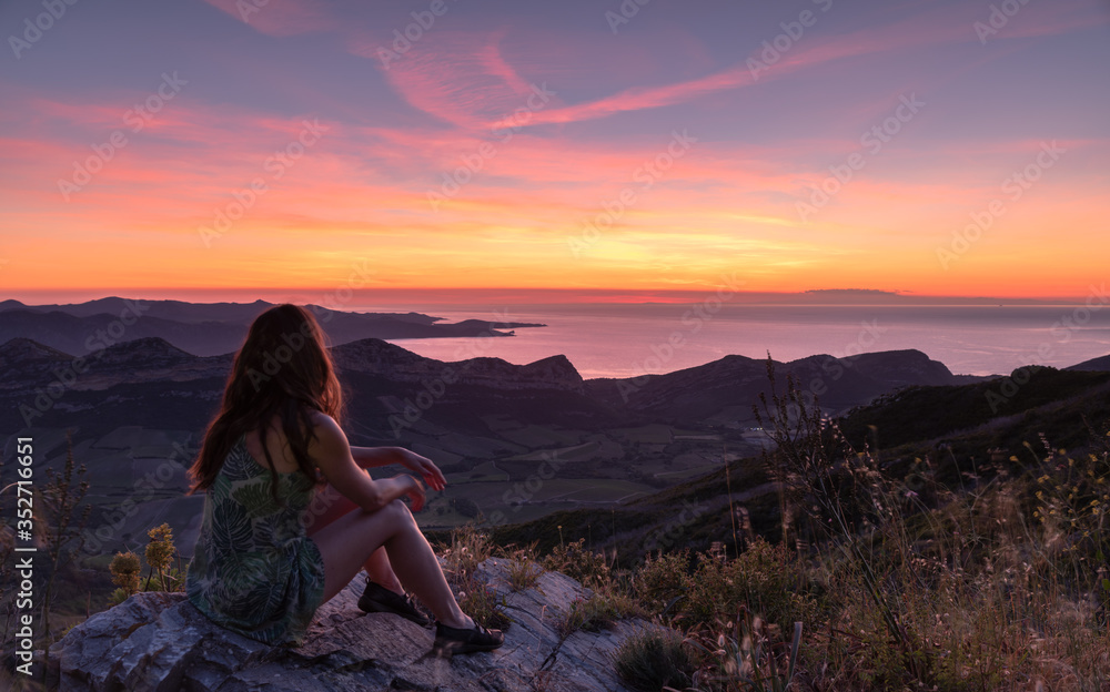 Woman sitting on a rock looking at the Sunset on the island of Corsica