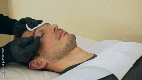 Close up of cosmetologist preparing man for the eyelash extension procedure. High quality close-up of a man laying on a couch during the esthetician lash treatment.
