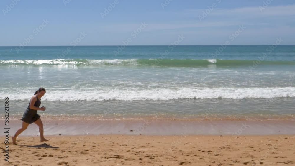 Woman on vacation running in front of beach waves in Algarve, Portugal Woman on vacation running in front of beach waves in Algarve, Portugal