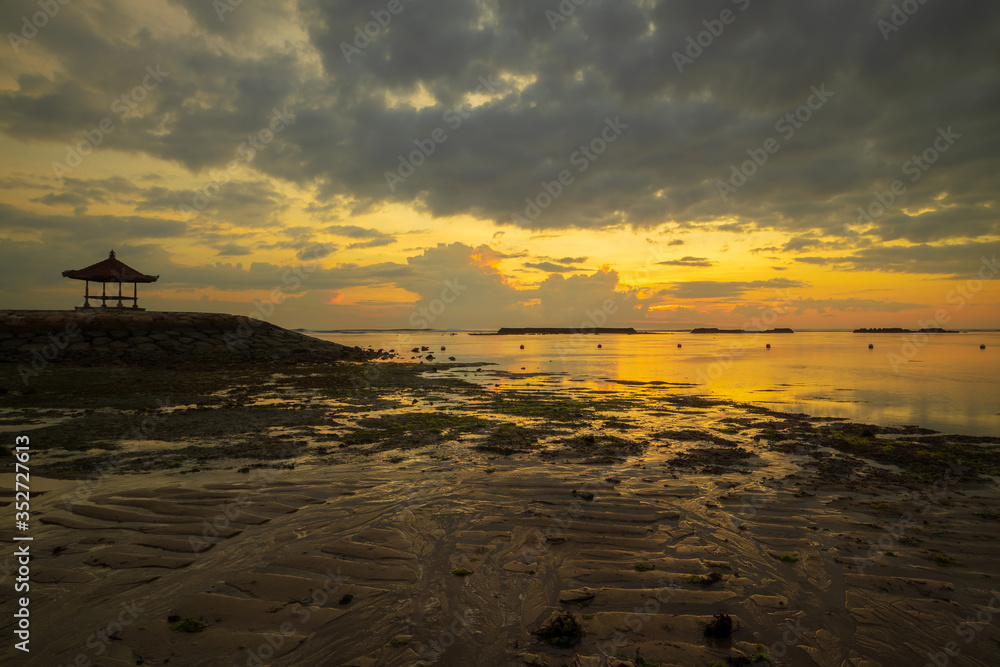 Sunrise seascape. Traditional balinese gazebo. Cloudy sky. Sunlight at horizon. Sandy beach during low tide. Nusa Dua beach, Bali, Indonesia. Sunrise seascape. Traditional balinese gazebo. Cloudy sky. Sunlight at horizon. Sandy beach during low tide. Nusa Dua beach, Bali, Indonesia.