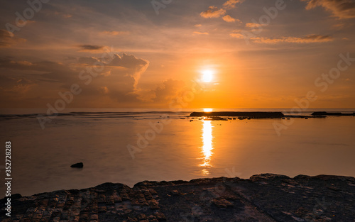 Rising sun at horizon. Sunrise seascape. Amazing water reflection. Cloudy sky. Sunlight at horizon. Nusa Dua beach, Bali, Indonesia. © Olga