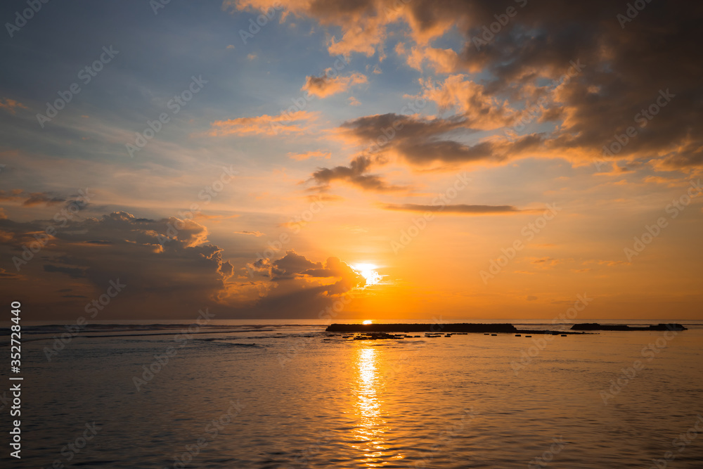 Rising sun at horizon. Sunrise seascape. Amazing water reflection. Cloudy sky. Sunlight at horizon. Nusa Dua beach, Bali, Indonesia.