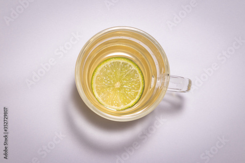 Chá de Camomila com Limão na xícara grande de vidro transparente com lindo vaso de flor amarela sobre a mesa branca