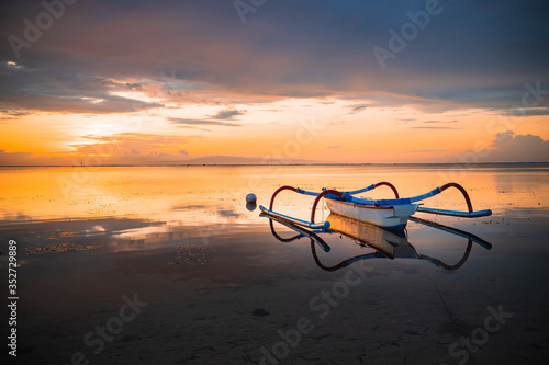 Seascape. Fisherman boat jukung. Traditional fishing boat at the beach during sunrise. Water reflection. Sanur beach, Bali, Indonesia.