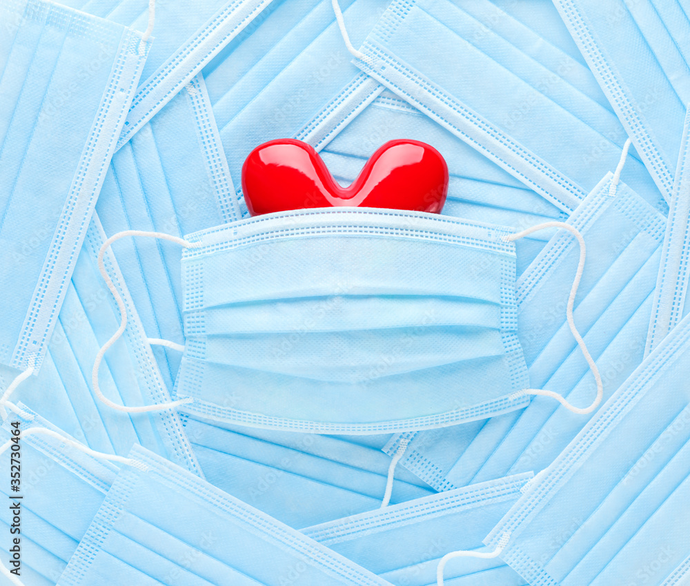 Bright red heart on a pile of medical face masks. Concept of support, love, care and a thank you to the frontline essential workers and healthcare workers. - obrazy, fototapety, plakaty 