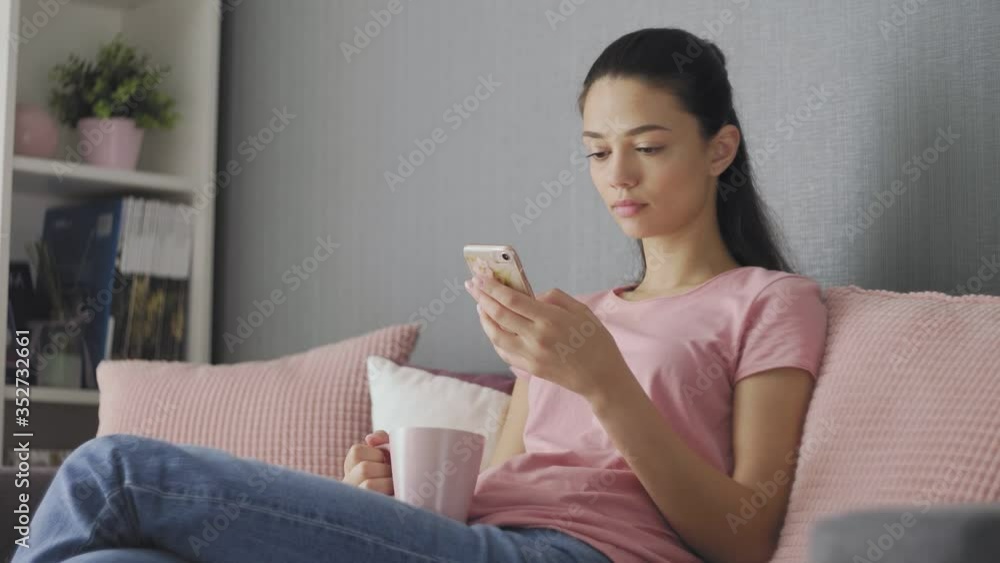 beautiful young woman using smartphone relaxing on couch at home browsing online texting drinking coffee enjoying comfortable lifestyle beautiful young woman using smartphone relaxing on couch at home browsing online texting drinking coffee enjoying comfortable lifestyle