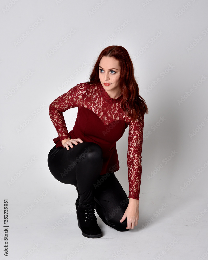 Portrait of a pretty girl with red hair wearing leather pants and long sleeved lace shirt. full length kneeling pose isolated against a studio background Portrait of a pretty girl with red hair wearing leather pants and long sleeved lace shirt. full length kneeling pose isolated against a studio background