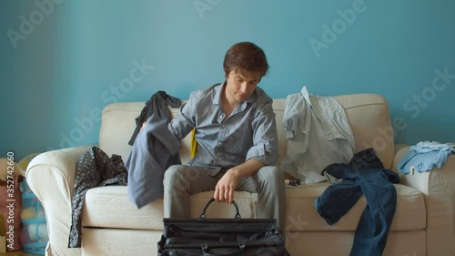Young handsome man sitting on the sofa and packing travel bag. Couple quarrel divorce
