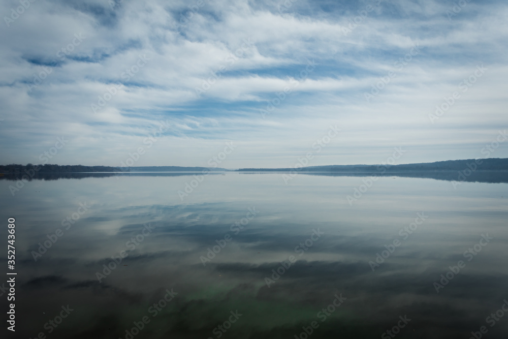 Reflections of Clouds in the Sky on calm, tranquil Water with Trees on Horizon and plenty of Copy Space