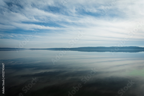 Reflections of Clouds in the Sky on calm  tranquil Water with Trees on Horizon and plenty of Copy Space