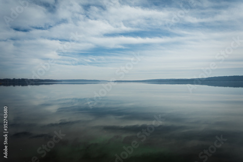 Reflections of Clouds in the Sky on calm  tranquil Water with Trees on Horizon and plenty of Copy Space