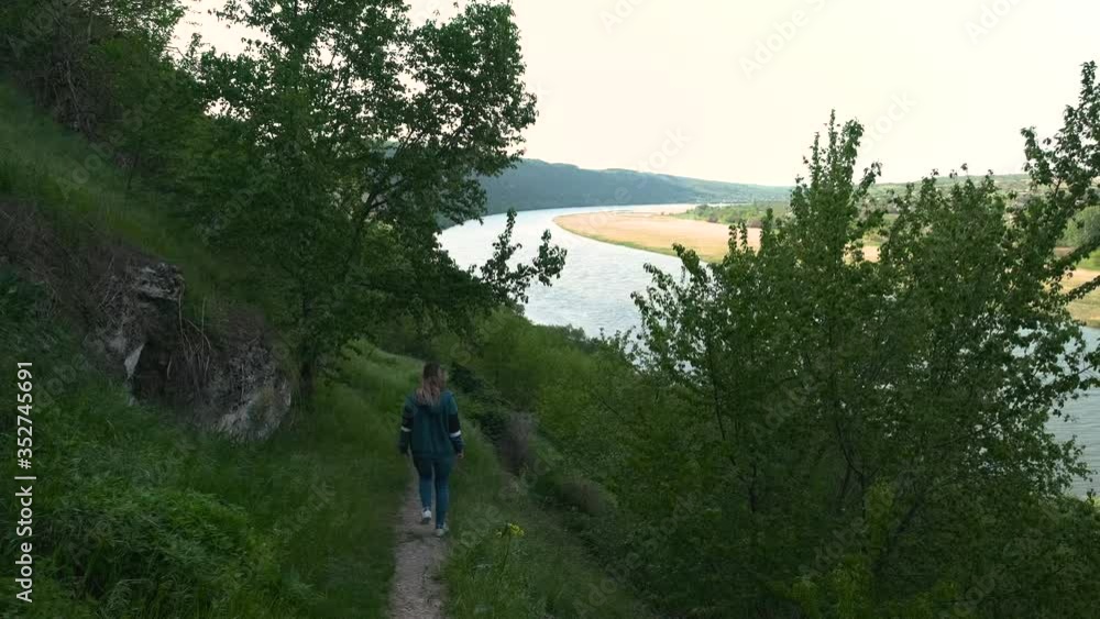 Girl walking down a riverbank on a green trail Girl walking down a riverbank on a green trail