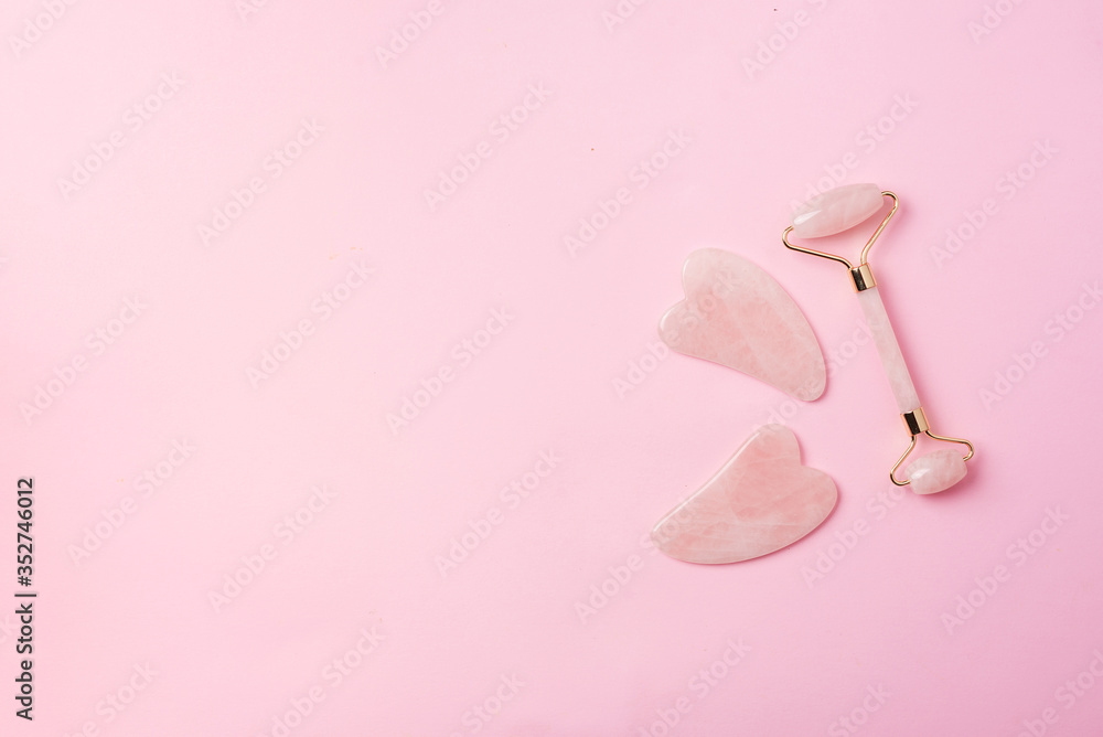 Pink gua sha facial massage roller. Anti age, lifting, toning face treatment at home. Skin care concept. Rose quartz stone roller on pink background. Copy space. Pink gua sha facial massage roller. Anti age, lifting, toning face treatment at home. Skin care concept. Rose quartz stone roller on pink background. Copy space.