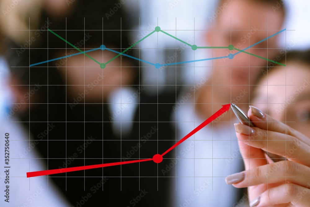 A group of people examines the financial statistics of an enterprise pointing with a hand with a pen on the graph point A group of people examines the financial statistics of an enterprise pointing with a hand with a pen on the graph point